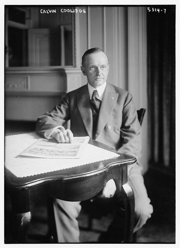 calvin coolidge sitting at desk in old photo